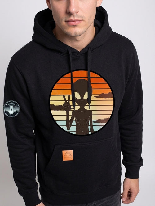 Black pullover hoodie with a large circular retro graphic on the chest showing a black alien silhouette against a sunset gradient, plus a small circular patch on the left sleeve.